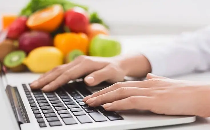 Woman typing on laptop with produce in background